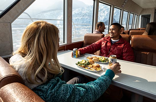 Two people sit for dinner at a window, looking out to glaciers in the sea.