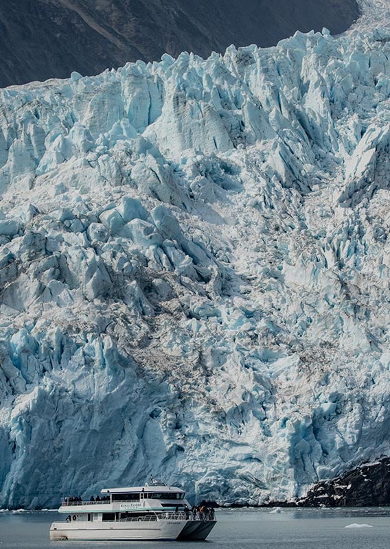 A boat cruises below a large tidewater glacier.