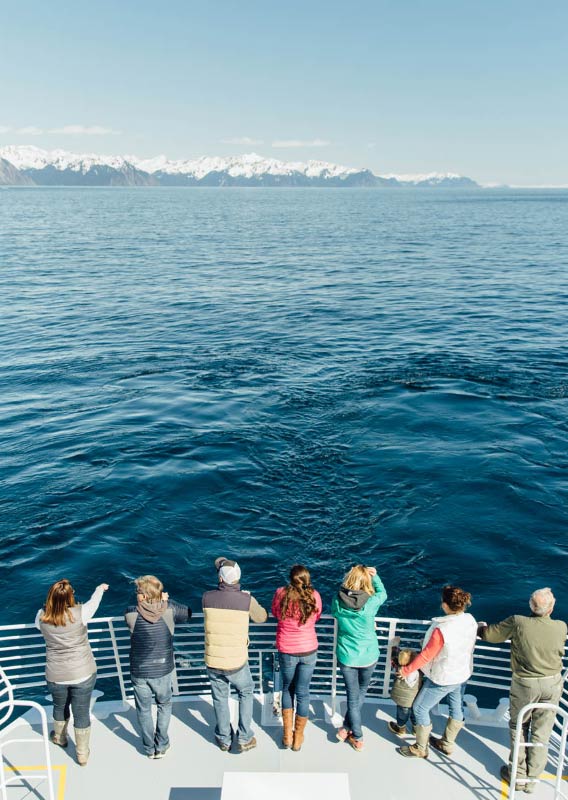 A crowd of people stand at the bow of a ship, viewing a glacier and mountains