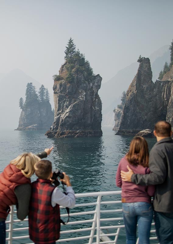 People stand at the guard rail of a tour boat looking out at rocky cliffs in the sea.