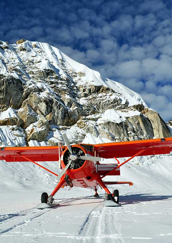 Red Airplane parked on snow beneath a snowy mountain