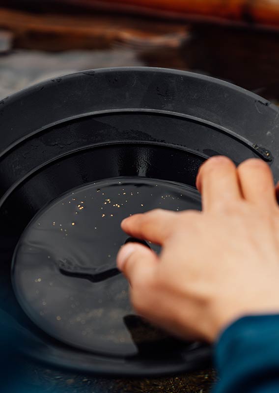 Close up of a hand sifting small flecks gold in a pan