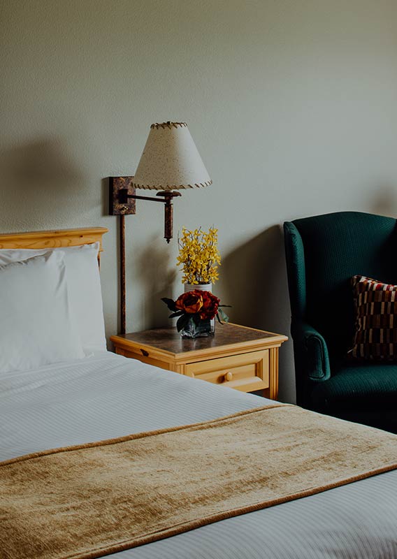 A hotel room with a wooden side table and dark green arm chair