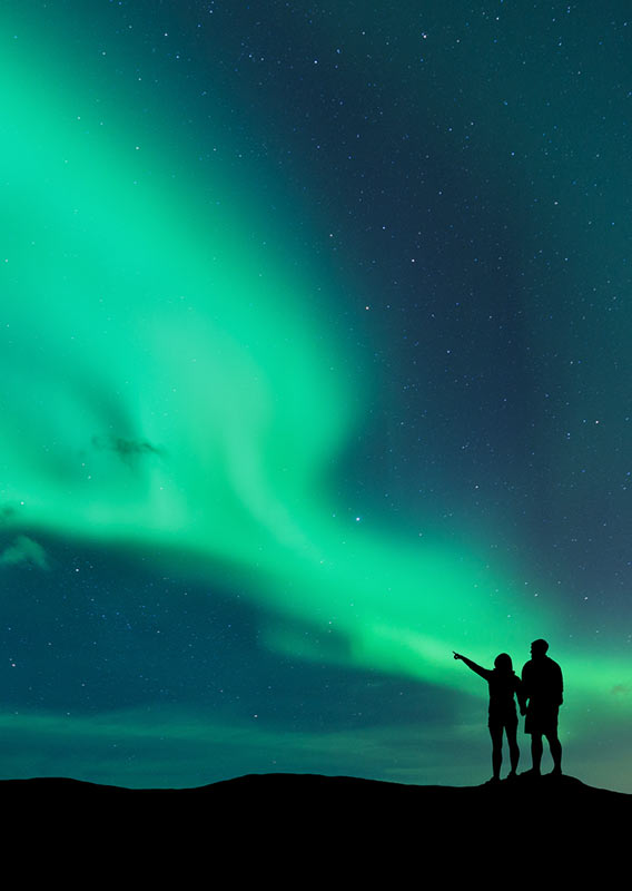 Two people stand silhouetted under impressive display of northern lights and starry skies