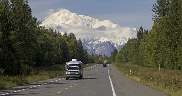 A view down a road towards a tall snow-covered mountains.