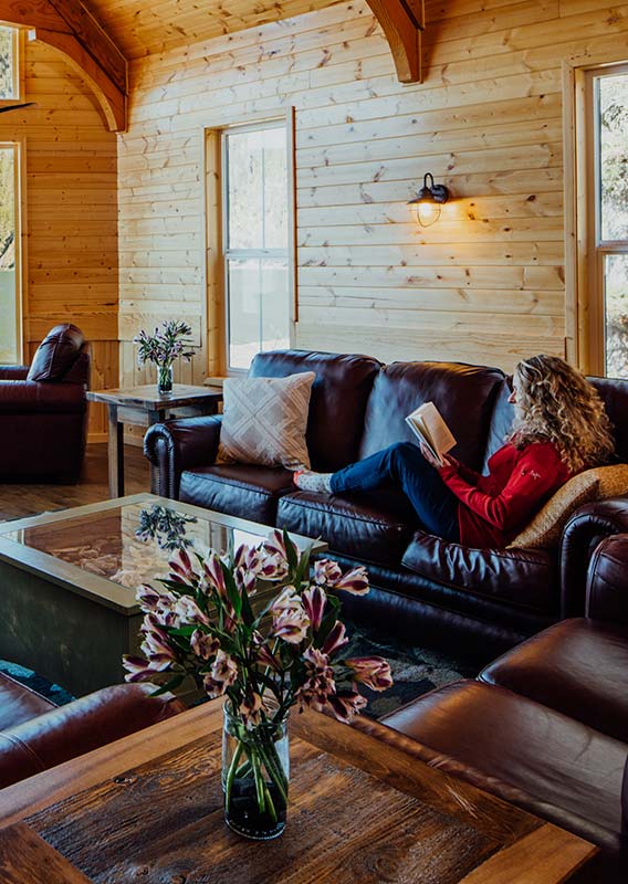 A guest relaxes on a sofa reading a book in a large wooden lodge overlooking the sea.