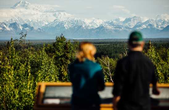 Two people standing on a balcony, looking at the mountains