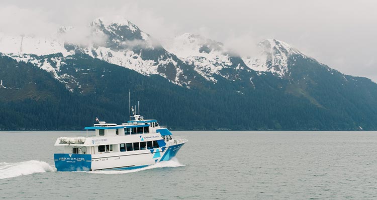 A boat cruises across the sea alongside tree-covered mountains.