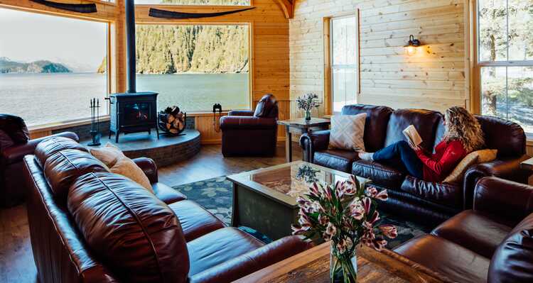 A guest relaxes on a leather couch in a wooden lodge overlooking the ocean.