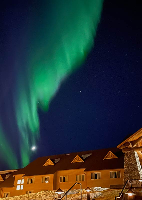 Green northern lights in the night sky above a wooden lodge building.