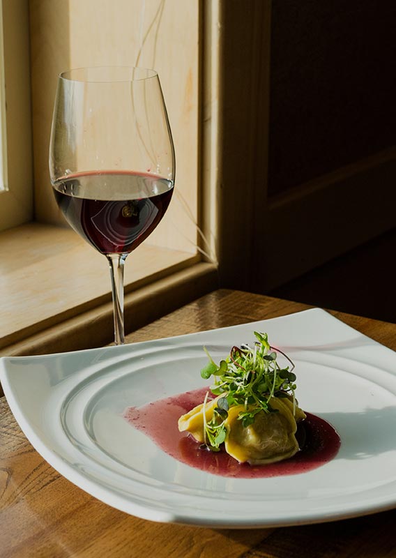 A dinner plate and a glass of red wine by a window.