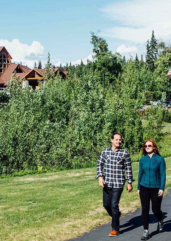 A couple walks outside in the summer with Talkeetna Alaskan Lodge in the back