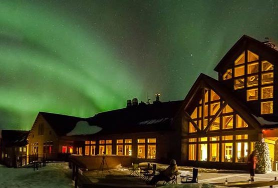 Green aurora in the sky above a large wooden lodge.
