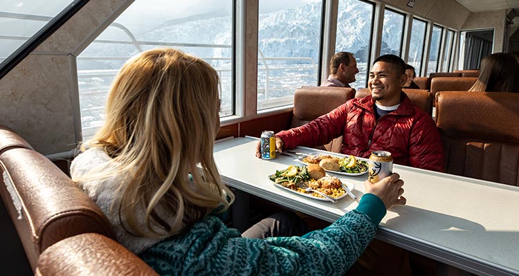 Two people sit for dinner at a windowside table on a boat.