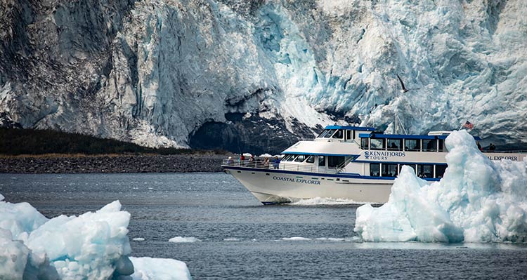 A boat cruises past icebergs and a seaside glacier.