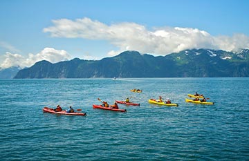 A group of sea kayakers on the water. There are mountains in the distance.