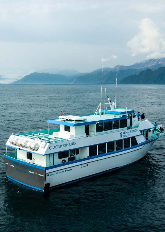 A tour boat on the sea, with coastal mountains in the distance.