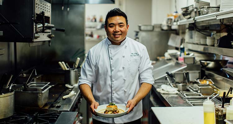 Chef Wes Choy posing in a kitchen holding a dish.